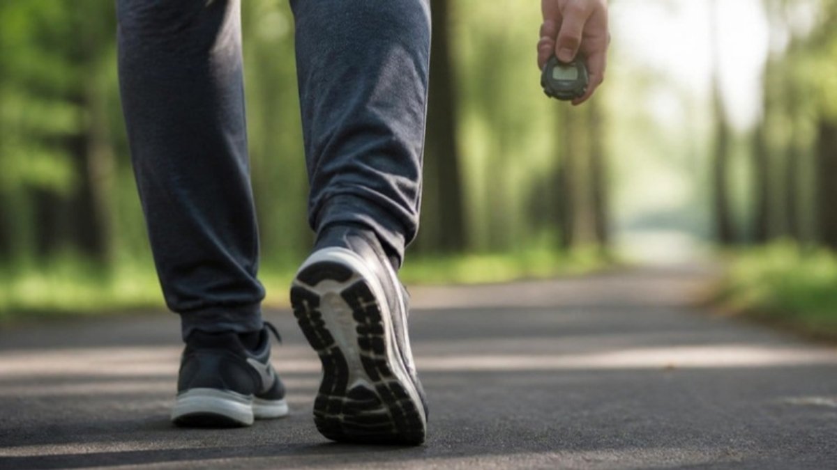 A pair of walking shoes on a paved path with a stopwatch resting beside them, in morning light