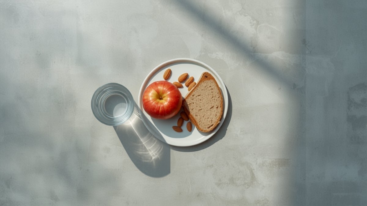 A plate with bread, an apple and almonds beside a glass of water, seen from above