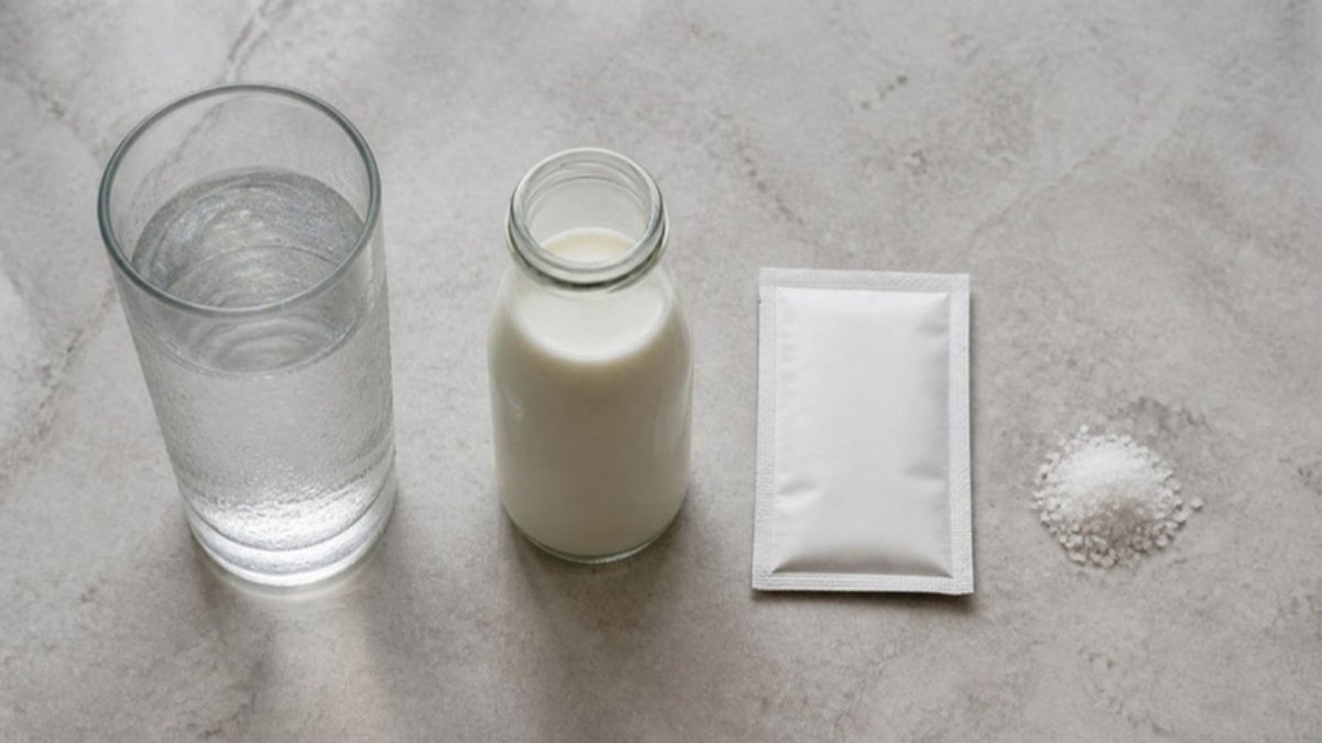 A glass of water, a small bottle of milk and a sachet of oral rehydration salts on a stone counter, seen from above