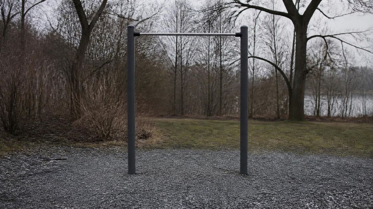 A plain steel pull-up bar between two posts in an empty outdoor exercise area on a grey morning, with gravel underneath